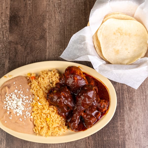 Chicken mole with rice, refried beans, and a side of tortillas on a wooden table.