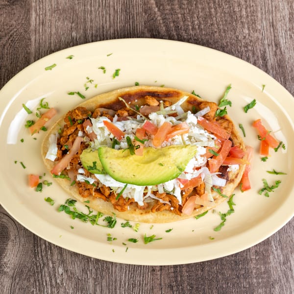 A sopes with chicken, lettuce, tomatoes, avocado, and cheese on a yellow plate.