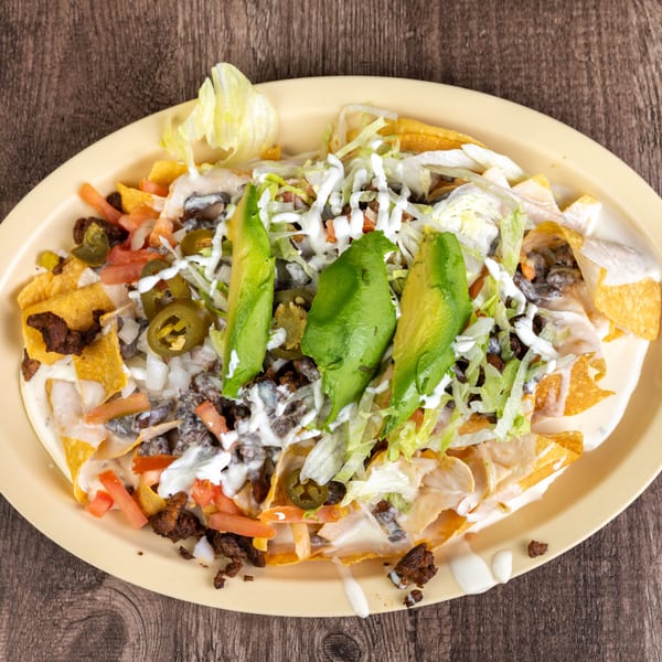 A plate of nachos with ground beef, cheese sauce, lettuce, tomatoes, jalapeños, and avocado slices.