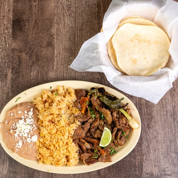 Carne asada plate with rice, refried beans, grilled pepper, and a side of tortillas.