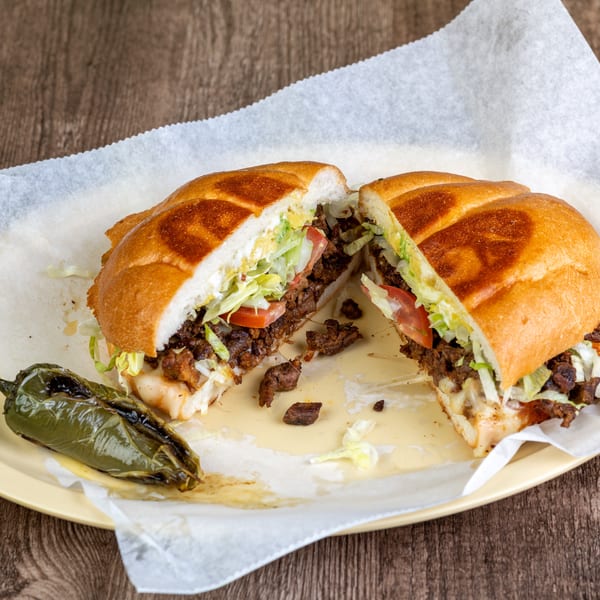 A torta sandwich, cut in half, filled with meat, lettuce, tomato, and cheese, served with a grilled jalapeño.